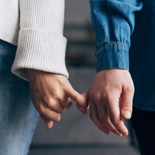 Händer zweier Personen, die die kleinen Finger eingehakt haben: Tastzellen in der Haut reagieren auf Druck oder Temperatur und unterscheiden zwischen bloßem Abtasten und zärtlichen Berührungen. 