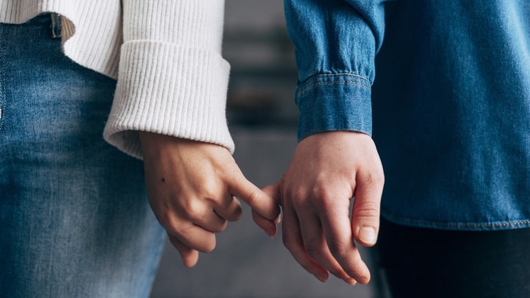 Händer zweier Personen, die die kleinen Finger eingehakt haben: Tastzellen in der Haut reagieren auf Druck oder Temperatur und unterscheiden zwischen bloßem Abtasten und zärtlichen Berührungen. 
