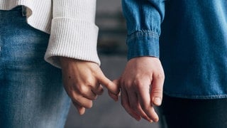 Händer zweier Personen, die die kleinen Finger eingehakt haben: Tastzellen in der Haut reagieren auf Druck oder Temperatur und unterscheiden zwischen bloßem Abtasten und zärtlichen Berührungen. 