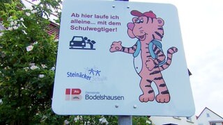 Auf einem Schild steht: "Ab hier laufe ich alleine... mit dem Schulwegtiger!" Das Schild soll gegen Elterntaxis helfen.