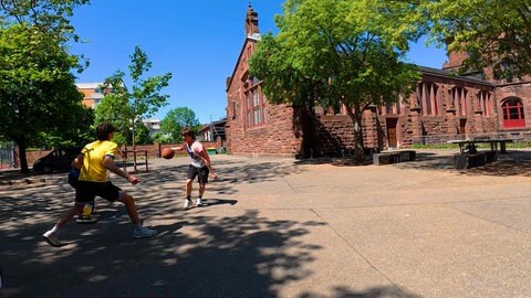 Eine Gruppe Jugendlicher spielt Basketball auf einem Schulhof.