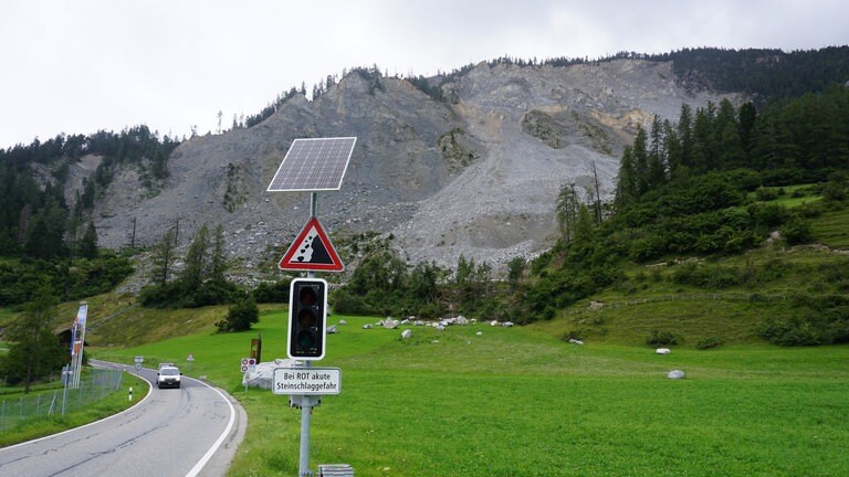 In der Nähe des Dorfes Brienz im Kanton Graubünden warnen Schilder vor Felsabgängen. Direkt am Dorfeingang steht das Schild “Bei Rot akute Steinschlaggefahr“, darüber eine Ampel. Wenn sie auf Rot springt, riskiert ein Autofahrer hier mehr als nur eine polizeiliche Verwarnung. Denn oberhalb des Dorfes erhebt sich ein Steilhang, von dem fast täglich Felsbrocken abbrechen und in Richtung Straße rollen. Einige besonders große liegen direkt neben der Straße.