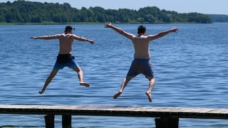 Zwei Jungen springen von einem Steg in einen See.