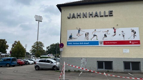 Außenansicht der Ulmer Jahnhalle. Ein Banner zeigt verschiedene Abteilungen des SSV Ulm 1846, die in Hallen unterkommen müssen. Der neue Sportpark soll hier Abhilfe schaffen.