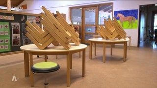 Raum in einem Kindergarten, wo Stühle auf Tischen liegen.