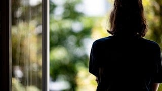 Silhouette einer Frau vor einem geöffneten Fenster.