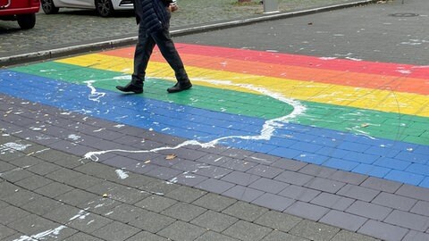 Menschen laufen über eine Zebrastreifen in den Farben des Regenbogens. In Mainz ist der Regenbogen-Zebrastreifen-mit-Farbe-beschmiert-worden