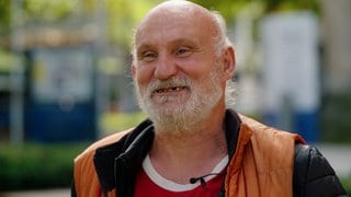 Harry Pfau steht vor „Harrys Bude” in Stuttgart und lächelt in die Kamera.
