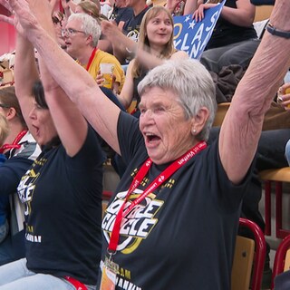 Hedwig Rheinbold, die bald 90-Jährige, reckt die Arme in die Luft zum Jubeln. Sie sitzt auf einer Tribüne.