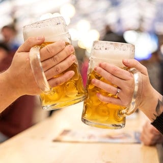 Ein Mann und eine Frau stoßen in einem Festzelt mit zwei Maß Bier an.