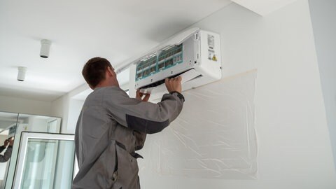 Ein Monteur befestigt das Innengerät einer Klimaanlage an der Zimmerwand