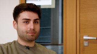 Junger Student mit braunen Haaren lächelt in die Kamera
