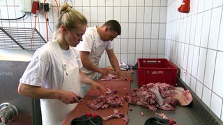 In einer Metzgerei in Lauffen am Neckar arbeiten Metzgerein Sonja und ein Mann in der Küche. Sie schneiden rohes Fleisch.