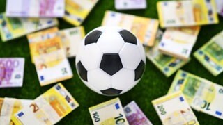 Ein Fußball liegt auf einem Rasen voller Geldscheine