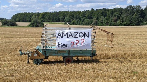 An einem Ladewagen, der mitten auf einem abgemähten Feld bei Bad Urach-Hengen (Kreis Reutlingen) steht, hängt ein Protest-Transparent gegen den Bau eines Verteilzentrums des Internet-Riesen Amazon auf dieser Fläche.