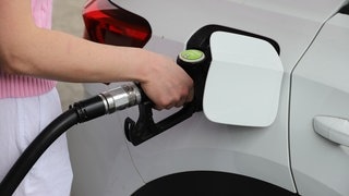 Frau steckt Zapfhahn in ihren Tank an einer Tankstelle