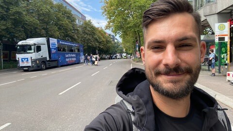 Loris Hoffmann steht vor einem Wagen, der am CSD Stuttgart 2025 teilnimmt.