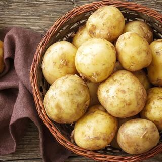 Pellkartoffeln mit Schale liegen in einem geflochtenen Korb auf einem Holztisch.
