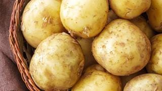 Pellkartoffeln mit Schale liegen in einem geflochtenen Korb auf einem Holztisch.