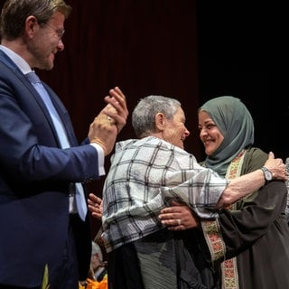 Marcus König (l-r), Oberbürgermeister der Stadt Nürnberg, klatscht, während sich Robi Damelin und Laila AlSheikh von der israelisch-palästinensische Versöhnungsinitiative Parents Circle – Families Forum (PCFF) umarmen.