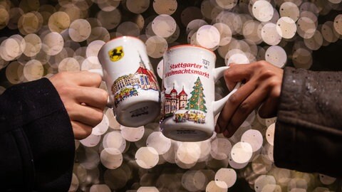 Zwei Menschen stoßen mit Glühwein auf dem Stuttgarter Weihnachtsmarkt 2022 an (Archivbild).