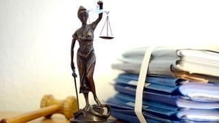 Auf einem Tisch liegen Gerichtsakten, ein Hammer und eine Statue der Justizia.