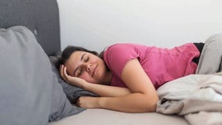 Eine Frau, die bequem im Bett schläft und gesunde Schlafgewohnheiten, Entspannung und gute Schlafhygiene zeigt.