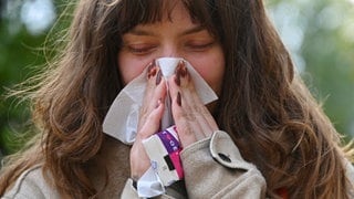 Eine Frau putzt sich in einem Park mit einem Taschentuch die Nase - mit dem Herbst beginnt die Zeit von Erkältung, Grippe und Corona.