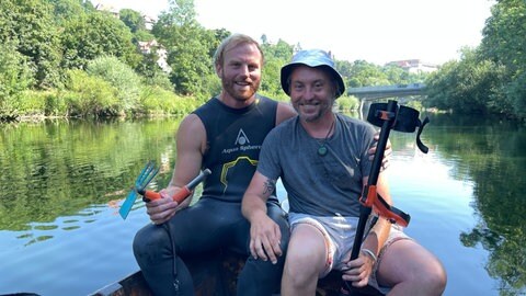 Jonas Hörrmann und Paul Schröter suchen nach einem Ehering im Tübinger Neckar. Sie sind mit einem Metallsuchgerät und einer Gartenhacke ausgestattet. 