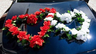 Zwei Blumenherzen schmücken eine Motorhaube. Die Polizei hat am Samstagabend einen Hochzeitskorso bei Nieder-Olm gestoppt, nachdem dieser den Verkehr massiv behindert hatte (Symbolbild).