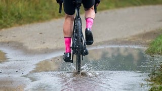 Neue Woche bringt Regen: Ein Mann fährt mit seinem Rennrad durch eine Pfütze. (Archiv)