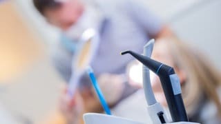 Ein Zahnarzt mit Mund-Nasen-Schutz und Schutzvisier versorgt eine Patientin in einer Praxis.