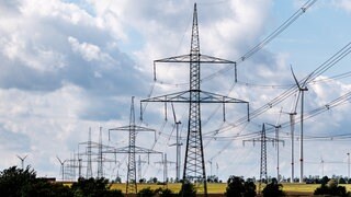 Hochspannungsleitungen und Windräder stehen in der Landschaft. Etliche Kommunen in BW haben nicht rechtzeitig ihren Stromverbrauch gemeldet.