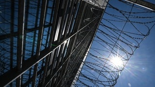 Gefängnismauer und -zaun von unten mit blauem Himmel. Die Polizei ermittelt gegen ein mutmaßliches kriminelles Netzwerk, das in der Justizvollzugsanstalt in Ravensburg mit Drogen gehandelt haben soll.