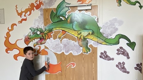 Auf der Eingangstür des "Drachenzimmers" ist ein feuerspeiender Drache abgebildet. Ein Junge will die Türe gerade öffnen. In diesem Zimmer können sich Kinder austoben, bis die starken Gefühle nachlassen.