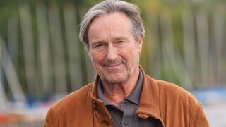 Helmut Zierl in brauner Lederjacke steht vor der Kamera und lächelt