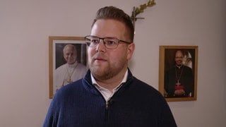Mann steht vor zwei gerahmten Bildern von Päpsten