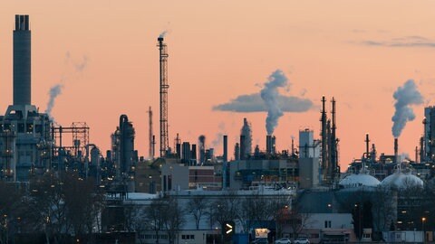 Rauchende Schornsteine der BASF in Ludwigshafen vor rötlichem Himmel.