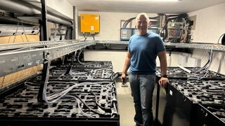 Unternehmer Jürgen Krüger steht bei seinen Akku-Blöcken im Keller der Firma