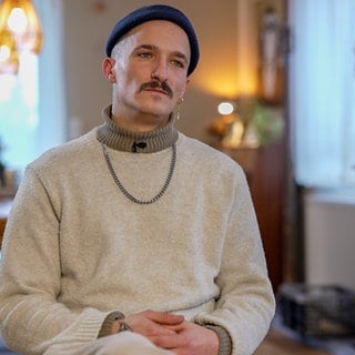 Junger Mann mit Mütze in einem Wohnzimmer auf einem Stuhl sitzend