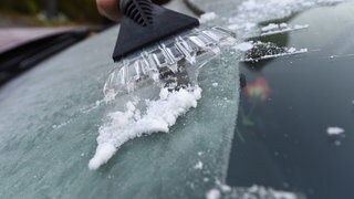 Mensch kratzt am frühen Morgen Eis von einer Autoscheibe