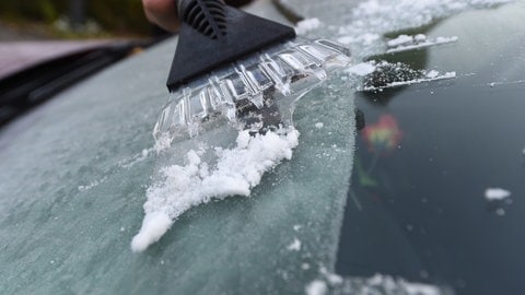 Mensch kratzt am frühen Morgen Eis von einer Autoscheibe