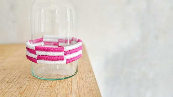 Vasen-Upcycling mit bunten Garnresten und kleinen Pompons zum Aufhängen