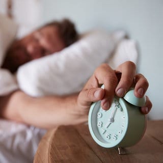 Ein Mann schaltet den Wecker neben seinem Bett aus. | Kleine Runde Sport gefällig? Wie wir durch Morgenroutinen fitter aus dem Bett kommen