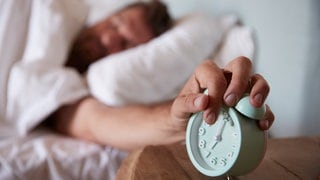 Ein Mann schaltet den Wecker neben seinem Bett aus. | Kleine Runde Sport gefällig? Wie wir durch Morgenroutinen fitter aus dem Bett kommen