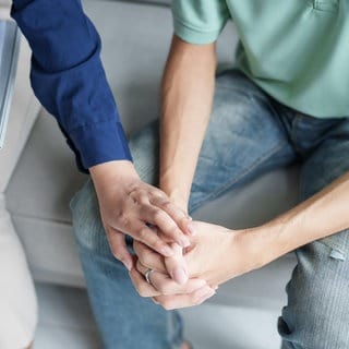 Eine Psychotherapteutin legt ihre Hand auf die Hand des Patienten
