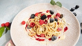 Auf einem Teller sind Flädle angerichtet als süße Variante mit Beeren, Vanillesauce und weißer Schokolade.