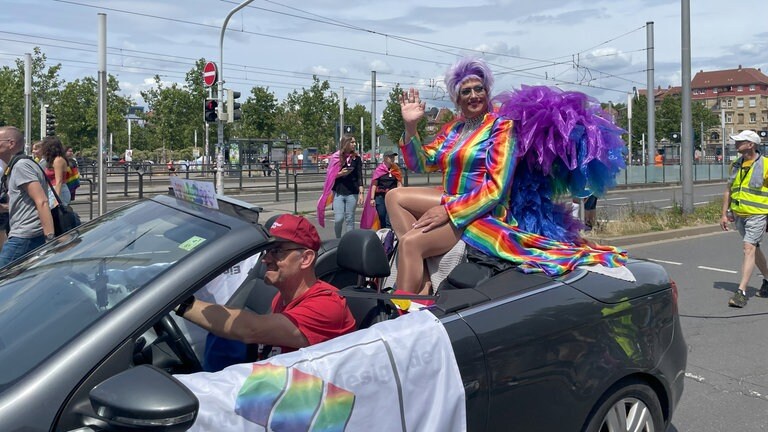 Drag-Queen sitzt im Cabrio und winkt