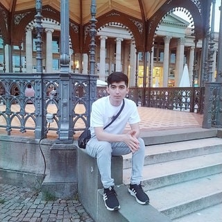 Sonatullah Uzbek sitzt auf eier Treppe in einem kleinen Park