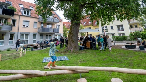 Mehrere Menschen stehen unter einem Baum an Tischen und Bänken. 